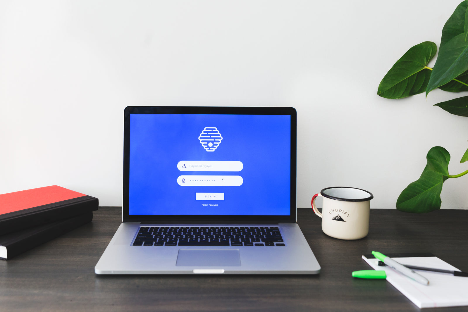 A laptop displaying a generic login form on a desk beside a mug and notebooks