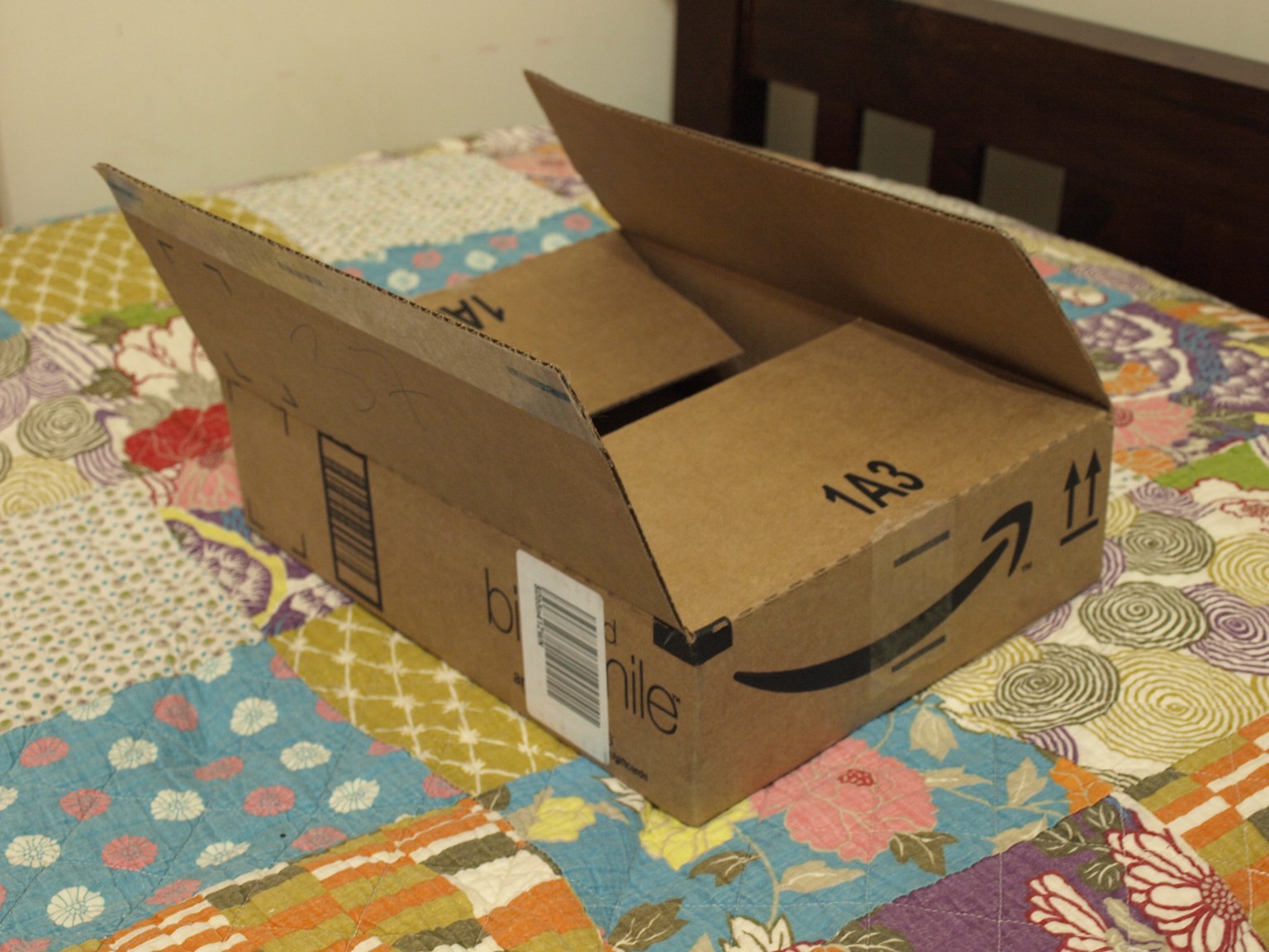 An open brown Amazon shipping box sits on a colorful patchwork quilt.