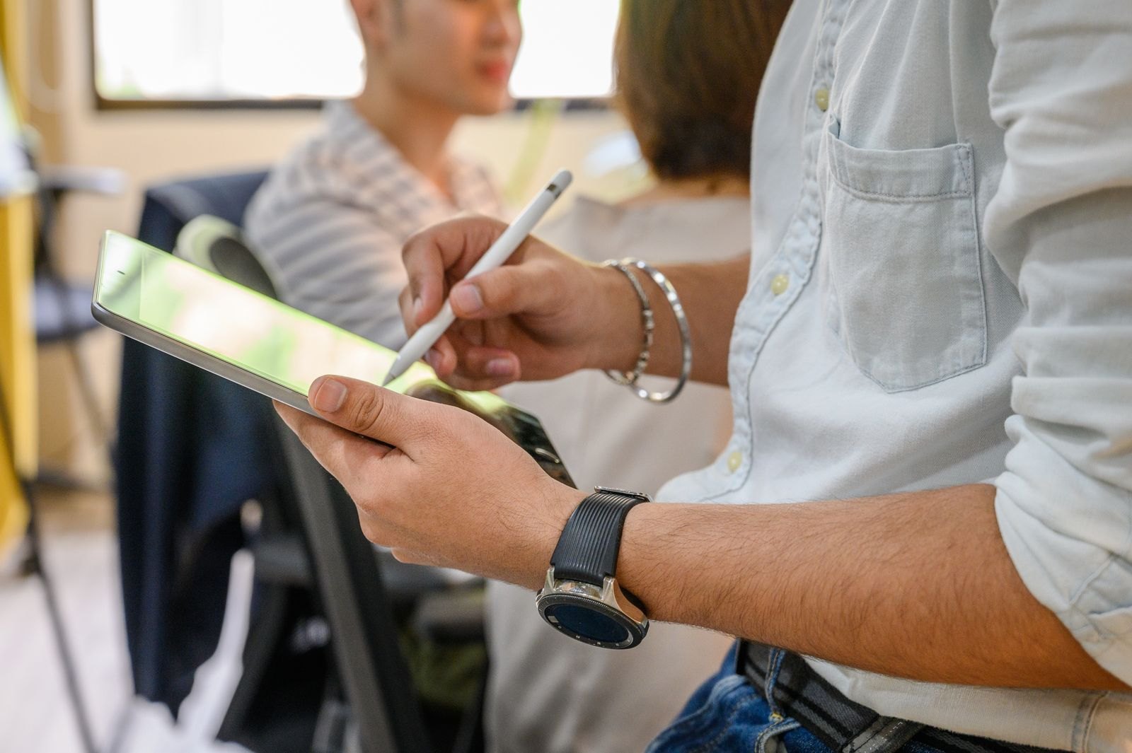 A person holds an iPad and writes on its screen with a white stylus.