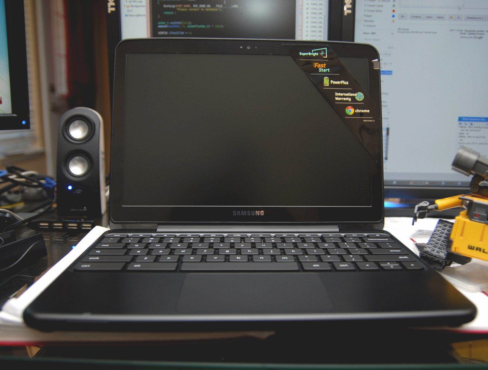 A Samsung Chromebook with a Chrome logo beside its dark screen, sitting on a desk.