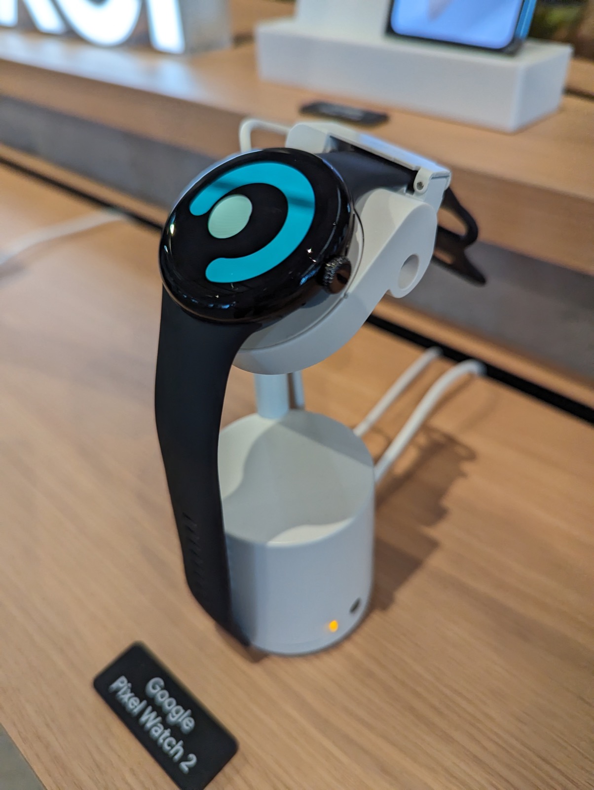 A Google Pixel Watch 2 with a black band on a white retail display stand.